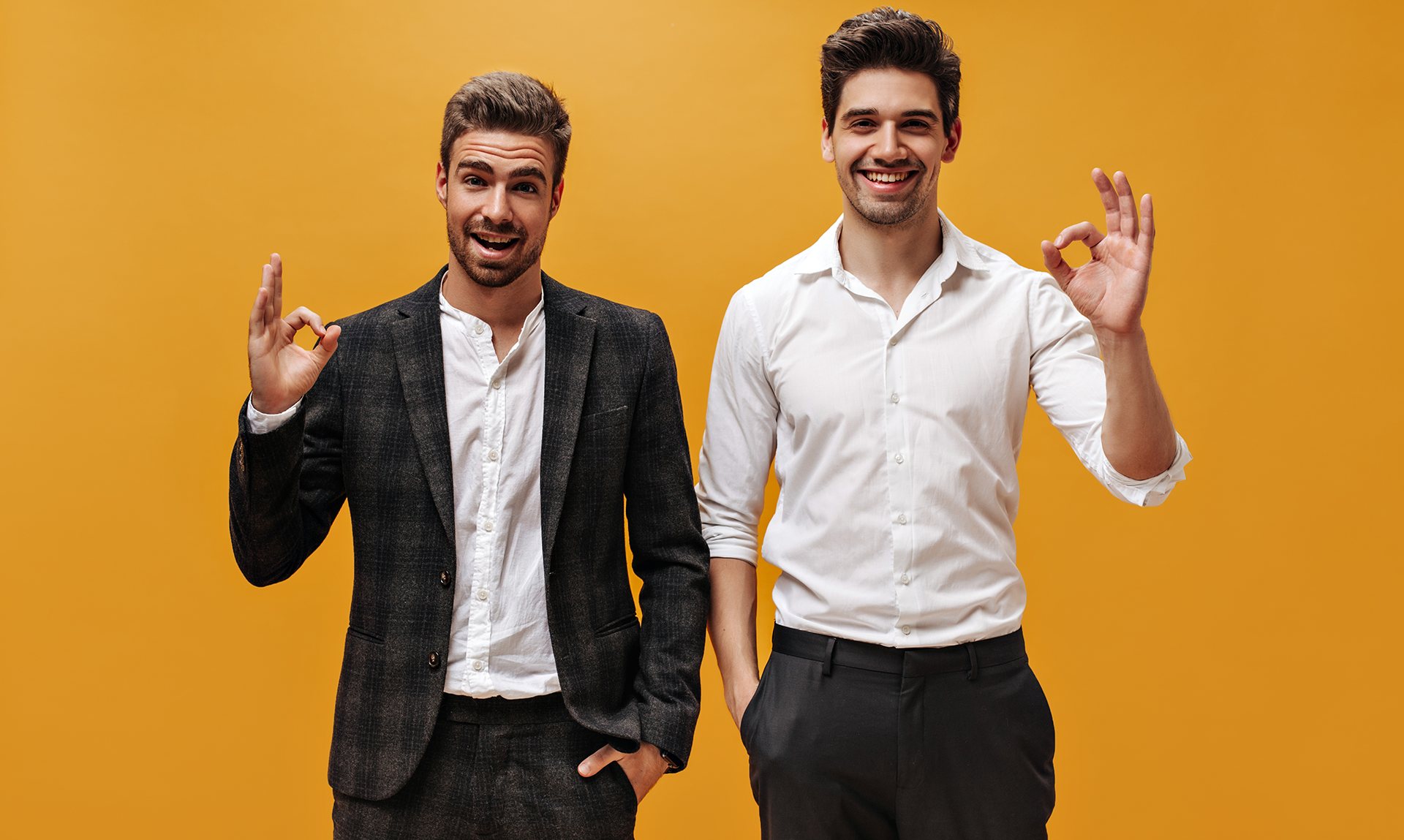 joyful-goodhumored-businessmen-white-shirts-black-pants-smile-sincerely-show-ok-signs-orange-isolated-background NWL 2